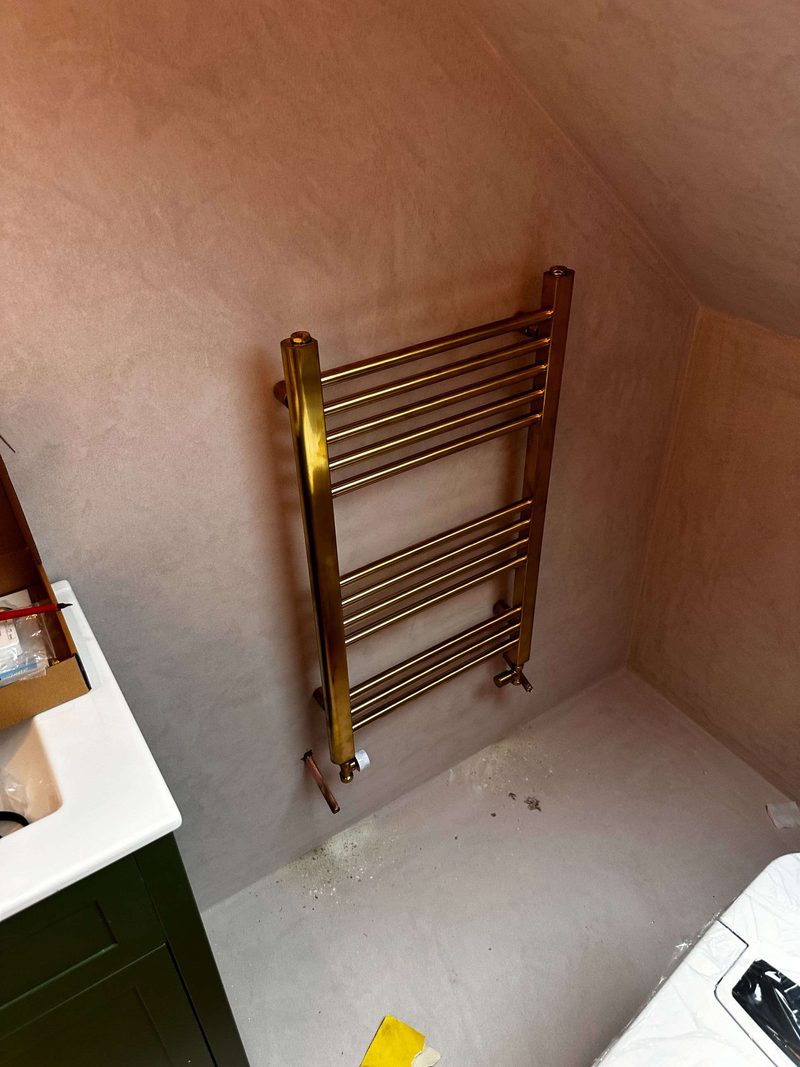 Brass heated towel rail mounted on a microcement bathroom wall, mid-installation