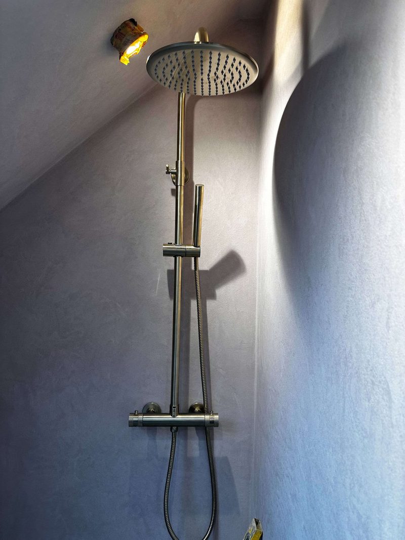 Brushed brass rainfall shower fitted on a microcement bathroom wall